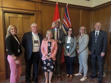 Group of professionally dressed people posing indoors with Canadian and British Columbia flags.