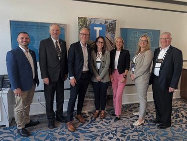 A group of seven professionals posing indoors in business attire.