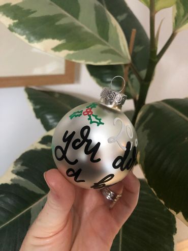 Silver glass bauble with wording "2020 you don't deserve a bauble" in black calligraphy with green a