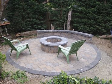 Outdoor stone fire pit with green chairs and a stone bench.