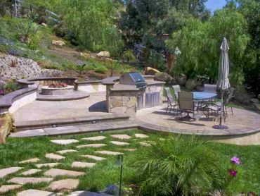 Outdoor patio with grill, fire pit, and dining area surrounded by greenery.