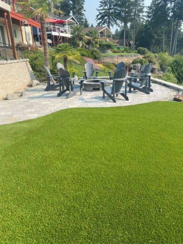 Outdoor patio with chairs around a fire pit and lush green lawn.