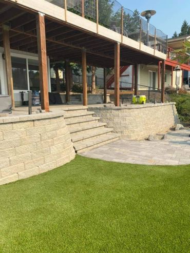 Modern backyard with stone retaining walls, steps, and artificial grass.