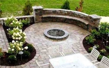 Curved stone patio with built-in seating and a fire pit surrounded by greenery.