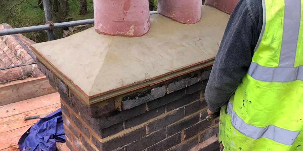 Worker in high-visibility vest near newly constructed brick chimney with clay pots.