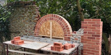 Partially built brick oven with scaffolding and construction materials outdoors.