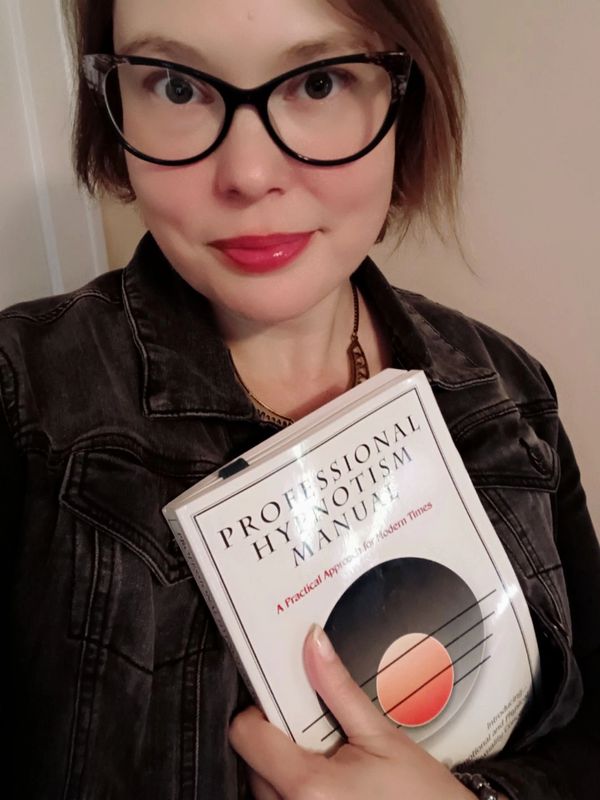 Person with glasses holding a book titled 'Professional Hypnotism Manual'.