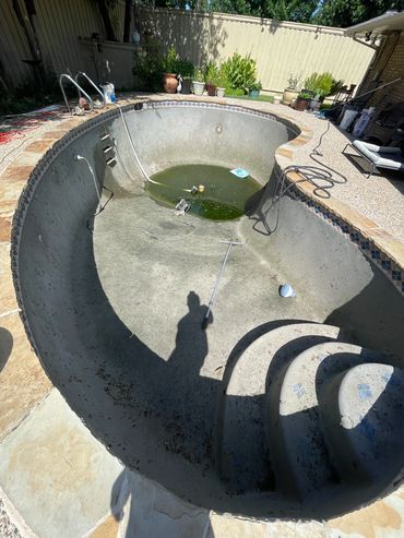 Empty, dirty swimming pool with some stagnant water and cleaning tools inside.
