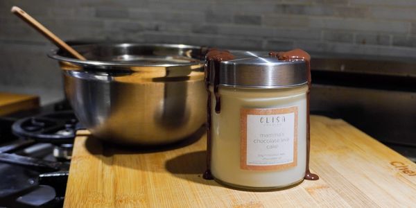 A candle labeled "mama's chocolate lava cake" with melted chocolate on the lid, next to a mixing bowl.
