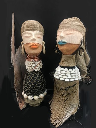 Two intricately decorated tribal dolls with shells and fabric.