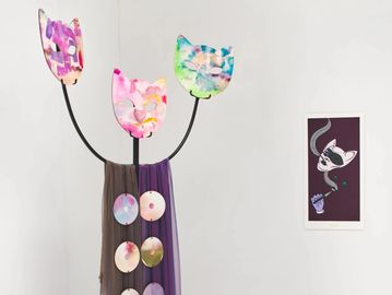 Art installation of colorful cat faces and hanging discs beside framed cat artwork.