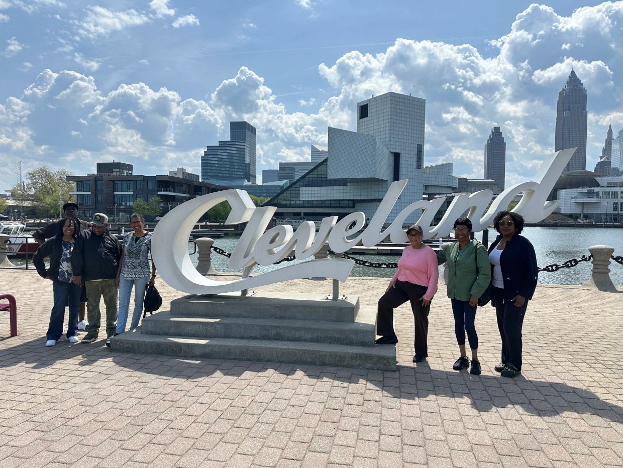 Group of people posing by the Cleveland sign on a sunny day.