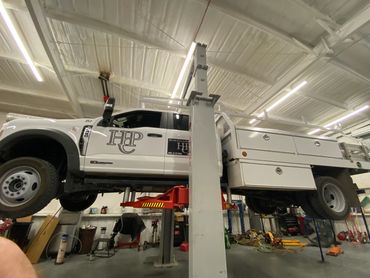 White utility truck lifted on a car lift in a garage.