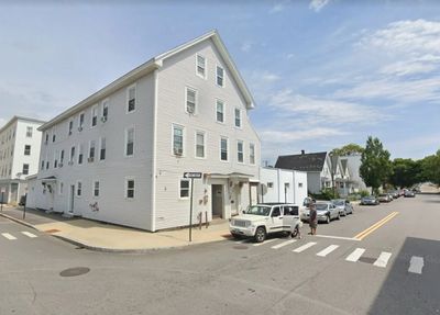White multi-story building on a street corner with parked cars.