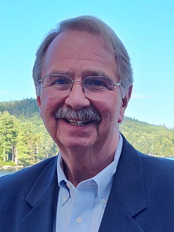 Smiling man with glasses and mustache outdoors.