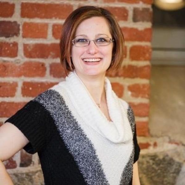 Smiling woman with glasses in front of a brick wall.