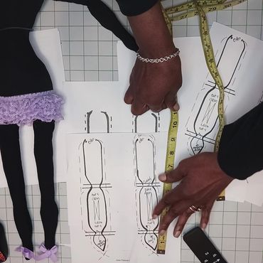 Hands measuring sewing patterns with a tape measure and fabric doll legs.