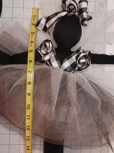 Black cloth doll dressed in tulle skirt with measuring tape beside it.