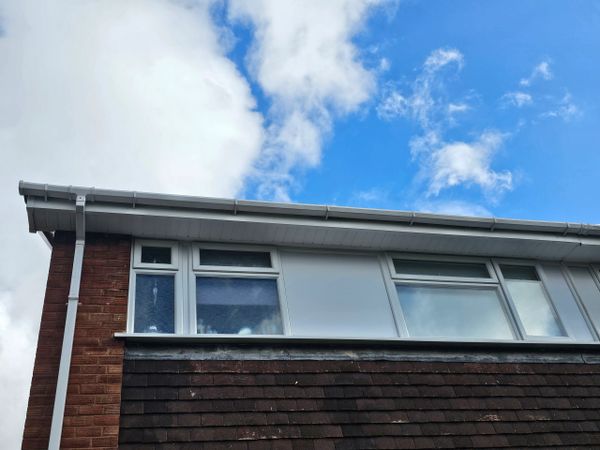 Upper story windows of a brick house under a partly cloudy blue sky.
