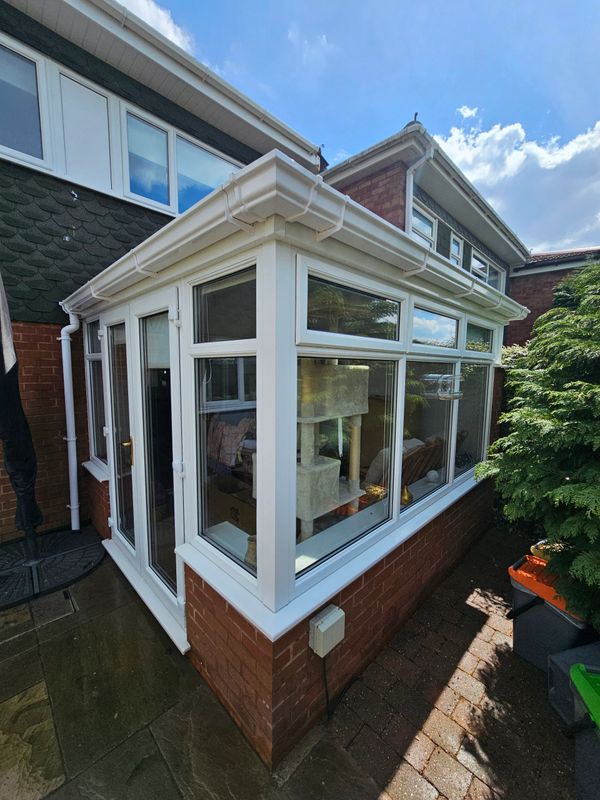 A sunlit conservatory attached to a brick house with white-framed windows.