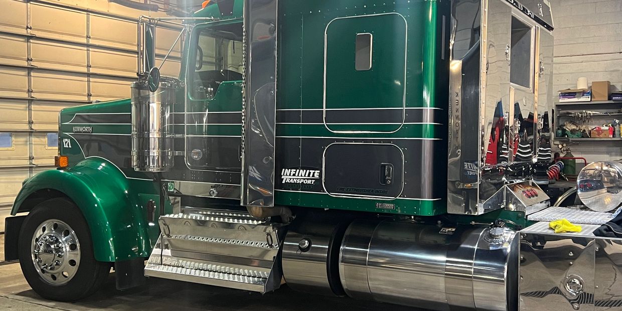 Green Kenworth semi-truck parked inside a garage with polished chrome details.