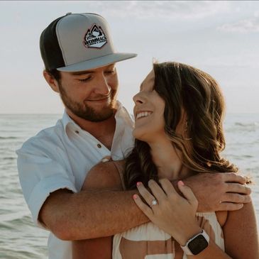 Couple sharing a loving moment by the sea, showcasing an engagement ring.