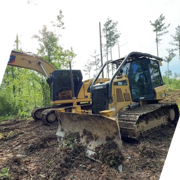 Two Caterpillar construction vehicles on a muddy forest clearing.