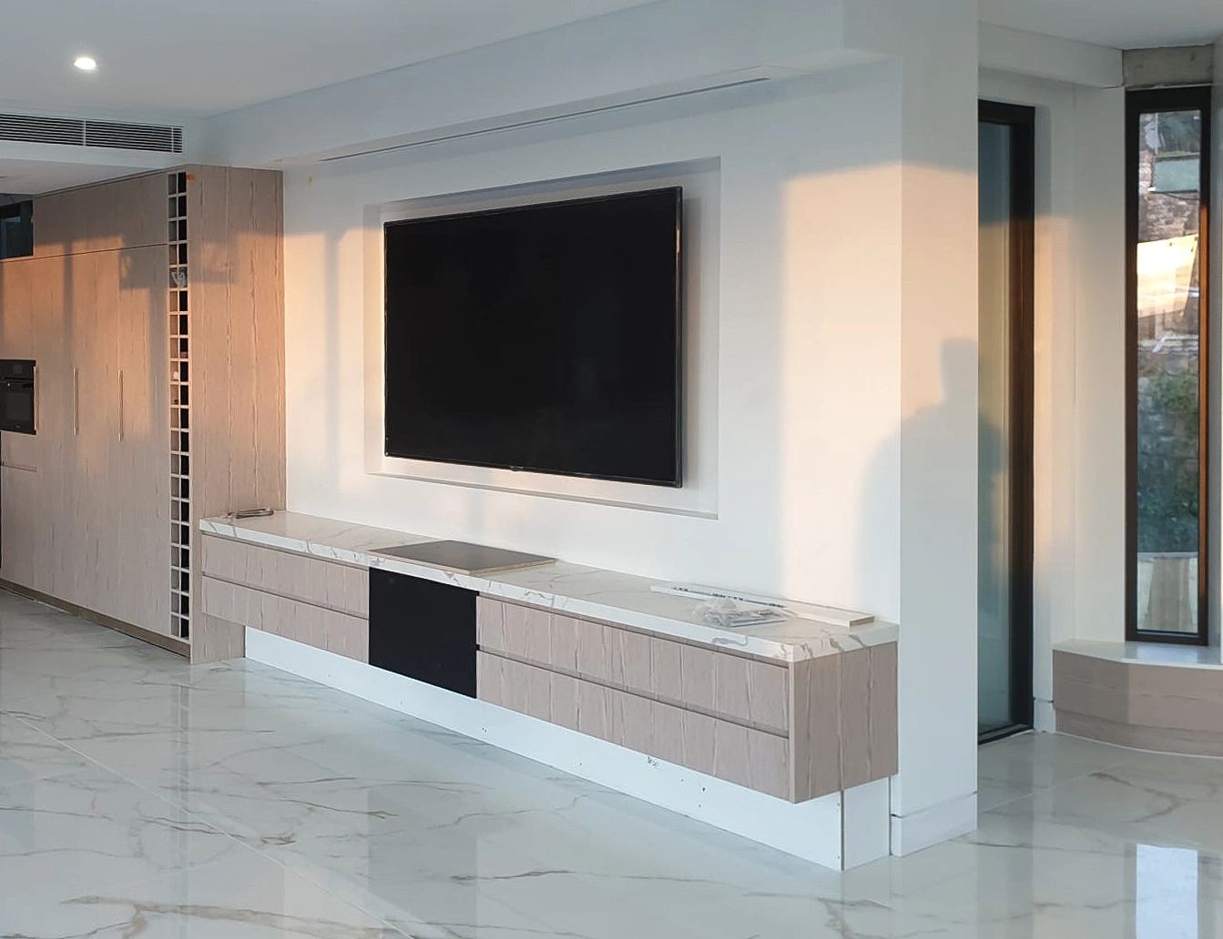 Modern minimalistic living room with wall-mounted TV and light wood cabinets.