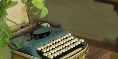 Old blue typewriter with plants nearby.