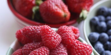 Fresh raspberries, strawberries, and blueberries in bowls.