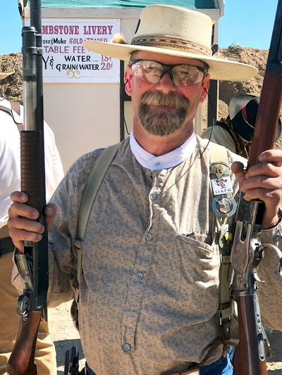 Man in vintage outfit holding two rifles.