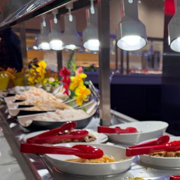 Buffet line with heat lamps, food trays, and red serving tongs
