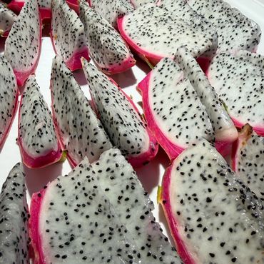 Slices of fresh white dragon fruit with pink skin and black seeds.