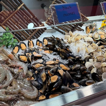 Chilled seafood bar with raw shrimp, mussels, and clams on ice.