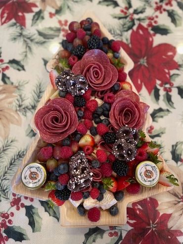 A festive Christmas tree-shaped charcuterie board with berries, salami roses, and chocolates.