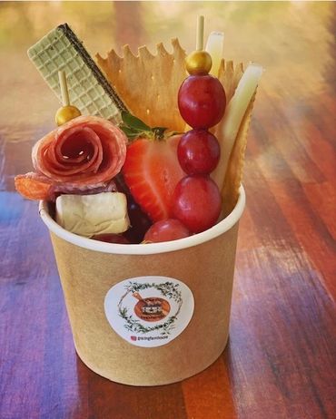 A creative snack cup with fruit, cheese, crackers, and cured meat on a wooden table.