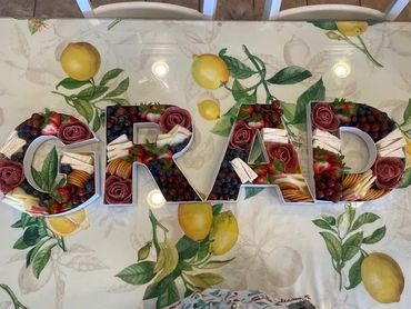 Charcuterie letters spelling GRAD on a lemon-patterned tablecloth.