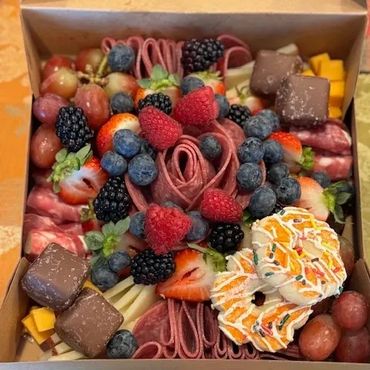 A colorful charcuterie box with fruits, meats, cheeses, and sweets.