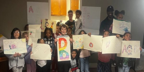 Children proudly display colorful drawings and artwork in a group photo indoors.