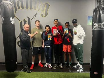 Group of six people posing with boxing gloves and books in a gym.