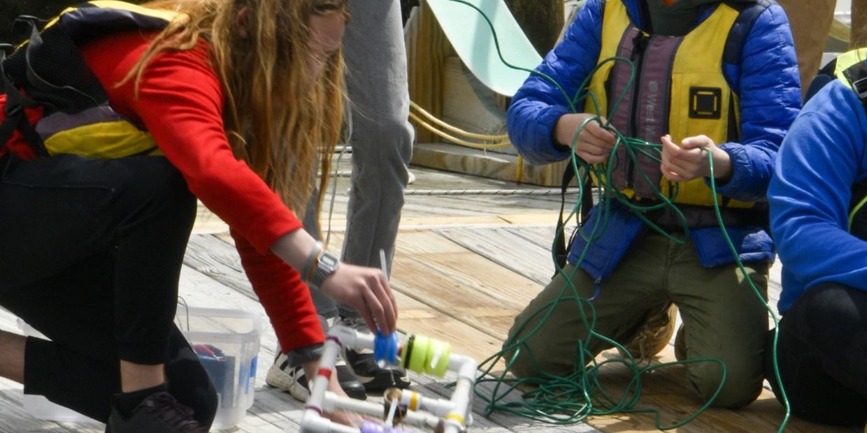 Children in life jackets handling equipment and ropes on a wooden dock.