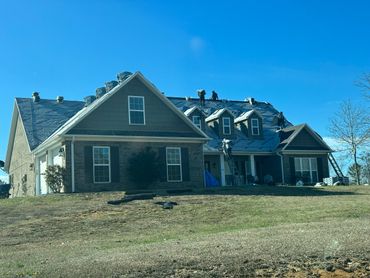 Workers are installing a new roof on a large suburban house under clear blue sky.