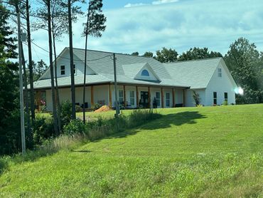 White countryside house with a large porch surrounded by greenery.