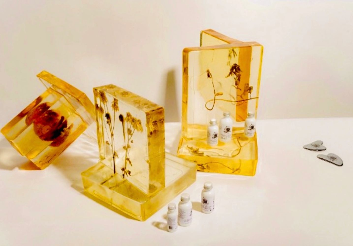 Decorative amber resin blocks with dried flowers and small white bottles.