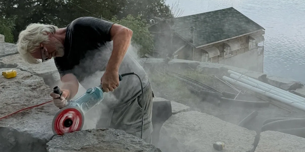 Man cutting stone with power tool near water.