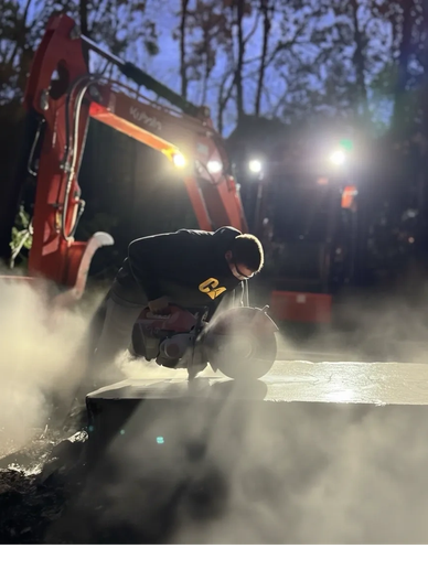 Person cutting stone with a saw at night, surrounded by mist and illuminated by machinery lights.
