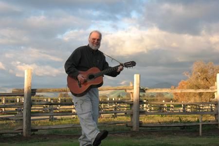A man playing a guitar while leaning on a fence