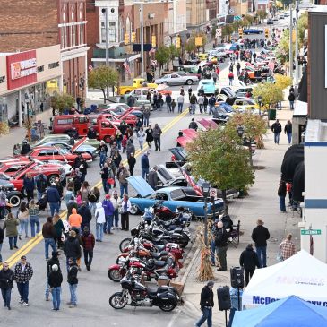 Crowded street car show with motorcycles and spectators.