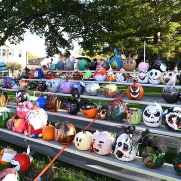 Rows of decorated pumpkins on bleachers outdoors.