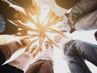 Group of friends joining hands in a circle, symbolizing unity and teamwork.